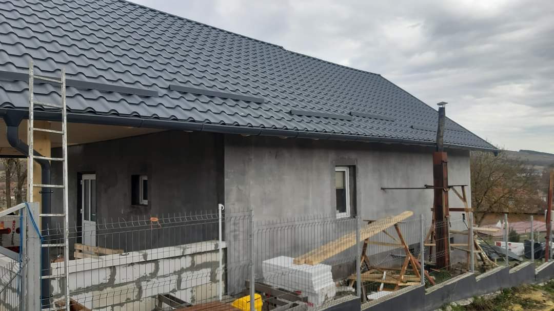 Casă nouă cu acoperiș din țiglă metalică gri și sistem pluvial